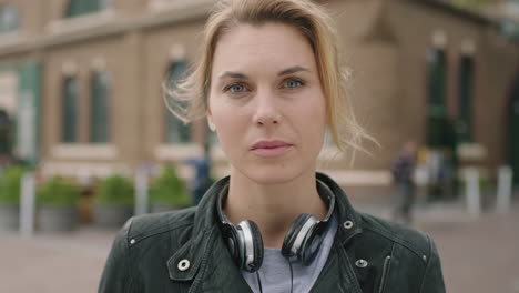 portrait of independent blonde woman looking serious staring intense wearing headphones on urban city background