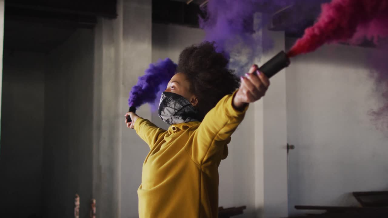 mujer de raza mixta sosteniendo bengalas azules y púrpuras de pie en un edificio vacío