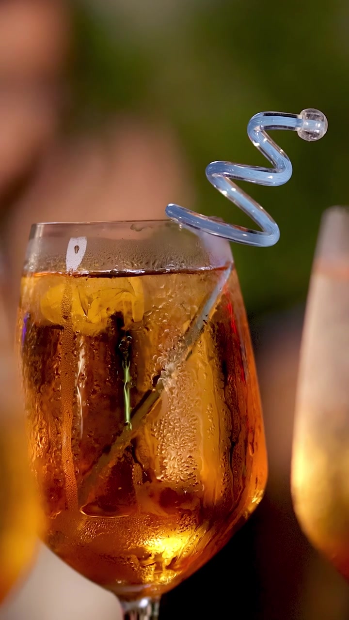 Primo piano di cocktail arancione con cannuccia a spirale, ghiaccio e condensa, all'aperto, con profondità di campo ridotta