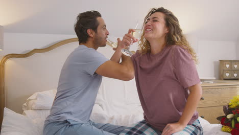 loving couple wearing pyjamas in bed at home celebrating birthday or anniversary with champagne