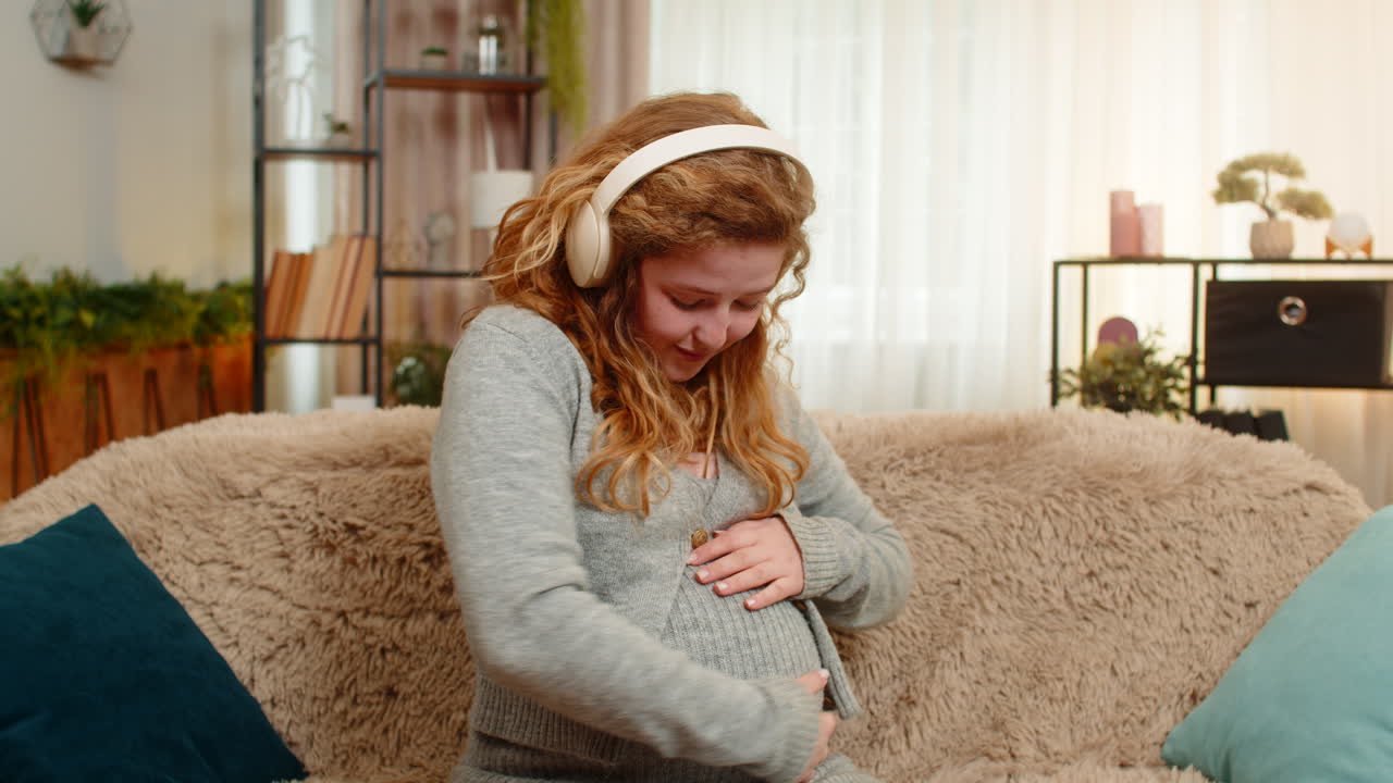 Pregnant young woman dancing with headphones gently touching belly smiling positive mood and energy