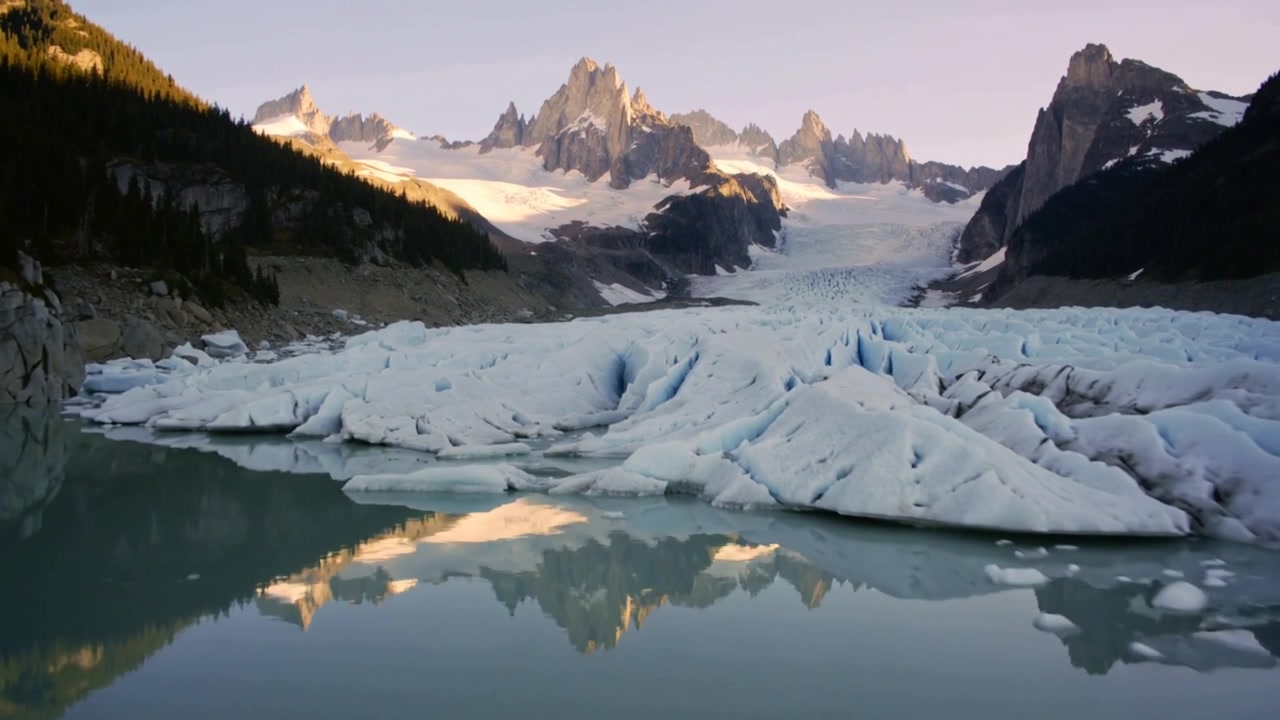 Pulling back, camera revealing glacier tongue meeting meltwater lake to show peak reflections