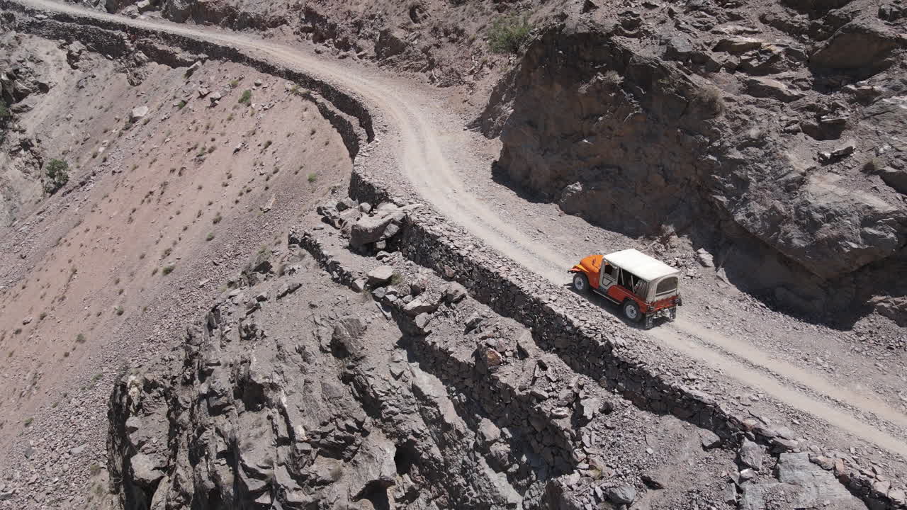 위험한 산길에서 이동하는 오프로드 차량의 공중 전망, 파키스탄 북부의 비포장 도로, 드론 샷