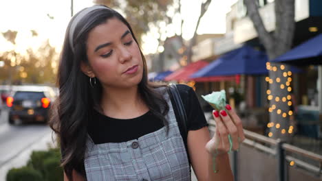 a beautiful young hispanic woman eating a messy, dripping ice cream cone dessert on the city street at sunset slow motion