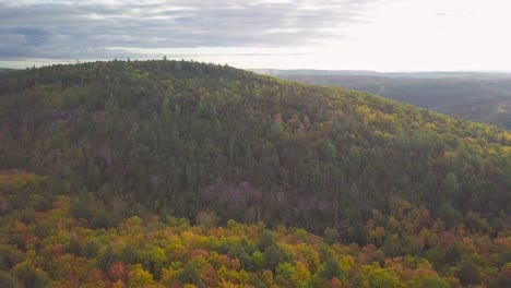 aerial daytime wide shot flying over fall forest colors orbiting a huge tall rocky cliff ridge and mist in kawarthas ontario canada