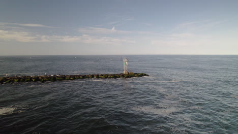 aerial drone shot pan around light house bouy on rock jetty as man fishes with heavy lens flare