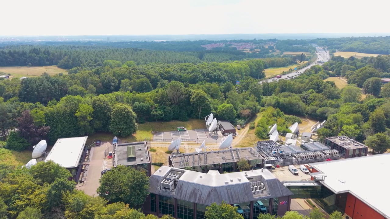 Right panning aerial shot over Southampton Science Park, Chilworth, revealing ten satellite dishes at the Sky broadcast campus surrounded by woodland and the M3 motorway.