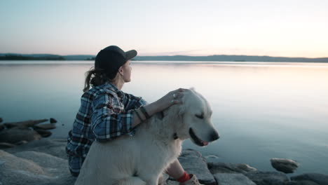 woman petting dog by lake at sunset