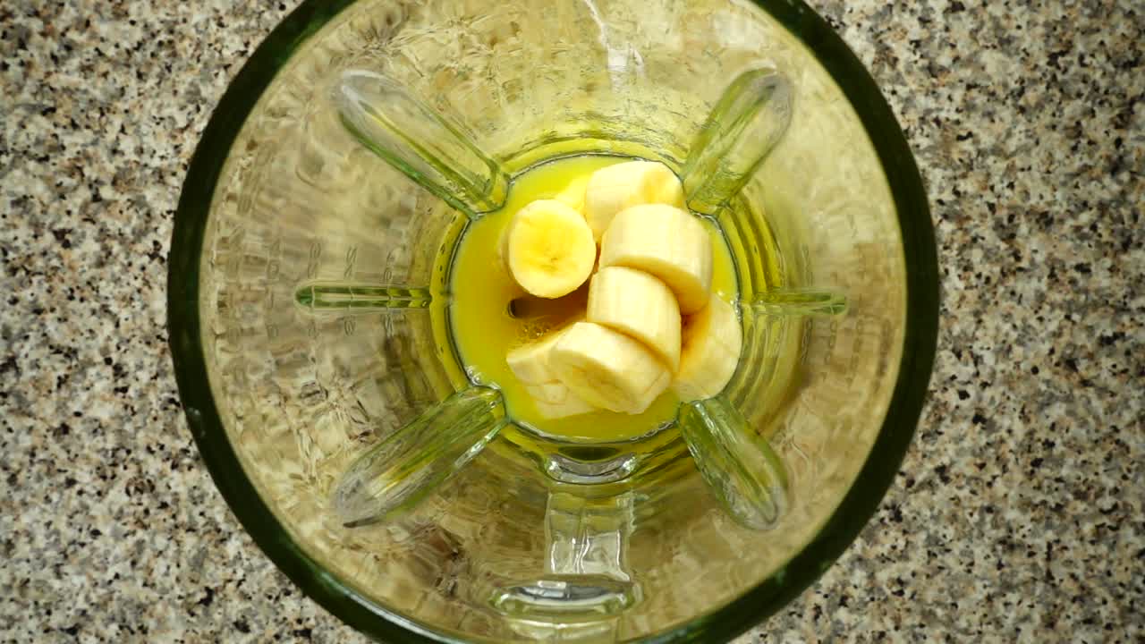 Pieces of apples fall in a blender bowl on pieces of bananas. Slow motion. Shooting in kitchen. Top view