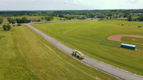 Yellow-ladder-firetruck-backing-up-on-street-by-fields-–-aerial-view-drone-orbit