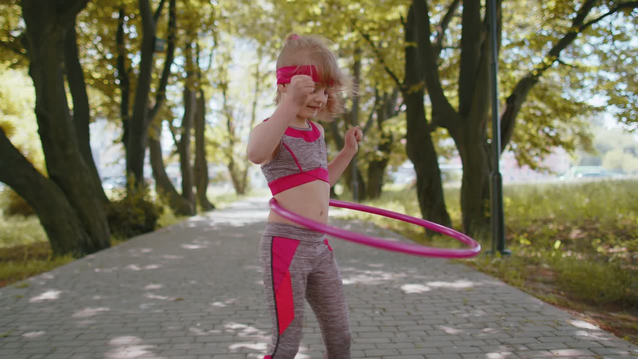 Bambina sportiva che si allena giocando a far ruotare un hula hoop attorno alla vita al parco