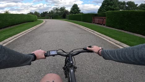 pov shot of a person cycling along a pristine road in an upscale neighborhood, surrounded by well-manicured lawns and lush greenery, showcasing the tranquility and exclusivity of the area