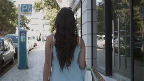 long-haired woman walking along street with shopping bags