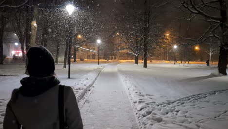 women walking alone at night on snow path in urban park of riga, latvia