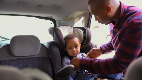 niño cansado sentado en el asiento del bebé, padre abrochando los cinturones de seguridad