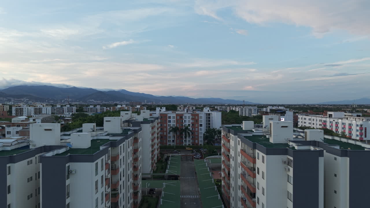 Drone video captures Valle de Lili's urban landscape at sunrise with mountains in the background. The bright sky enhances the city's beauty from above, showcasing tranquility