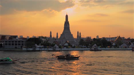 bangkok,wat arun temple during golden hour from a distance,boats crossing in front of the majestic chao phraya river.still frame.