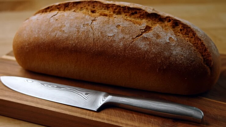 Rustic Loaf On Wooden Cutting Board, Closeup Highlighting Golden Crust And Flour Dusting Beside Stainless