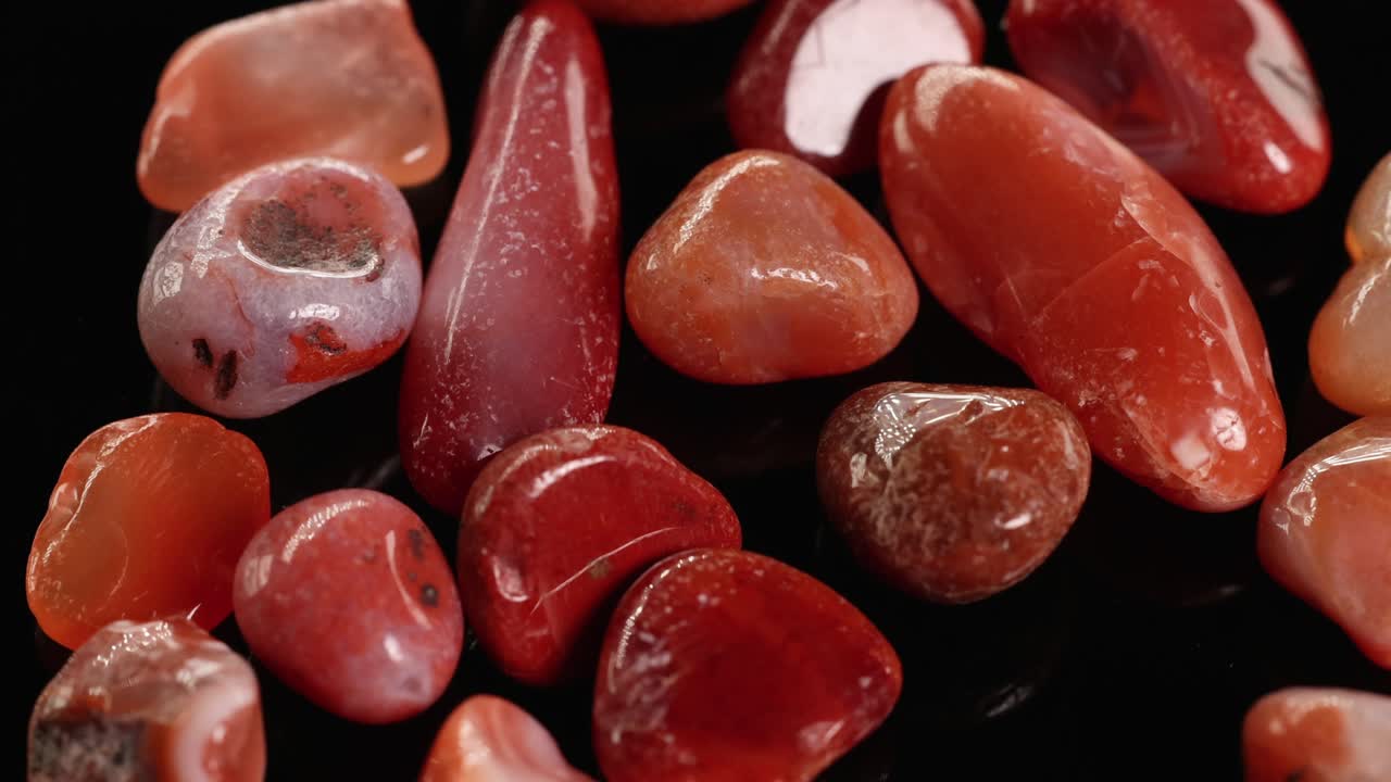 Red jasper stones slowly rotate against a black background, highlighting their smooth textures and vibrant colors