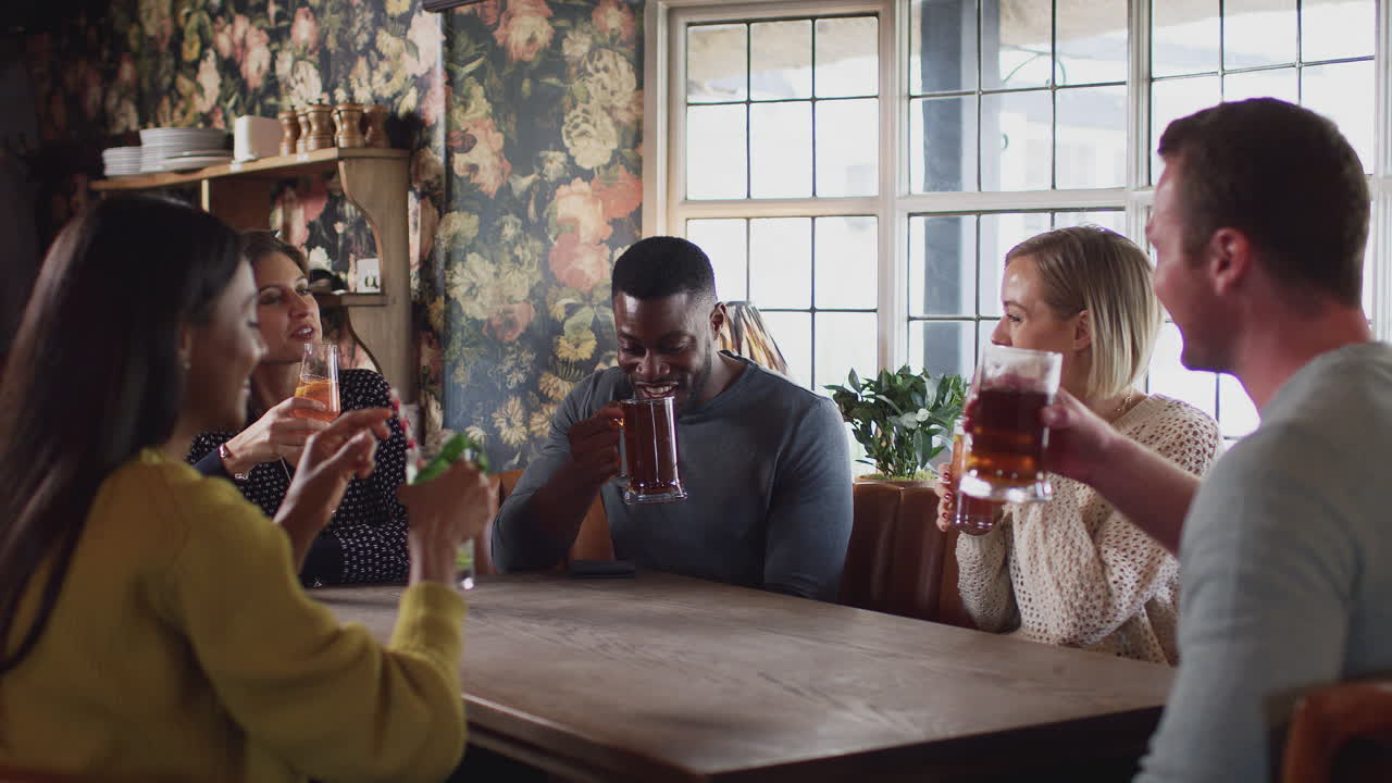 grupo de amigos haciendo brindis mientras se reúnen para tomar una copa a la hora del almuerzo en un pub inglés tradicional