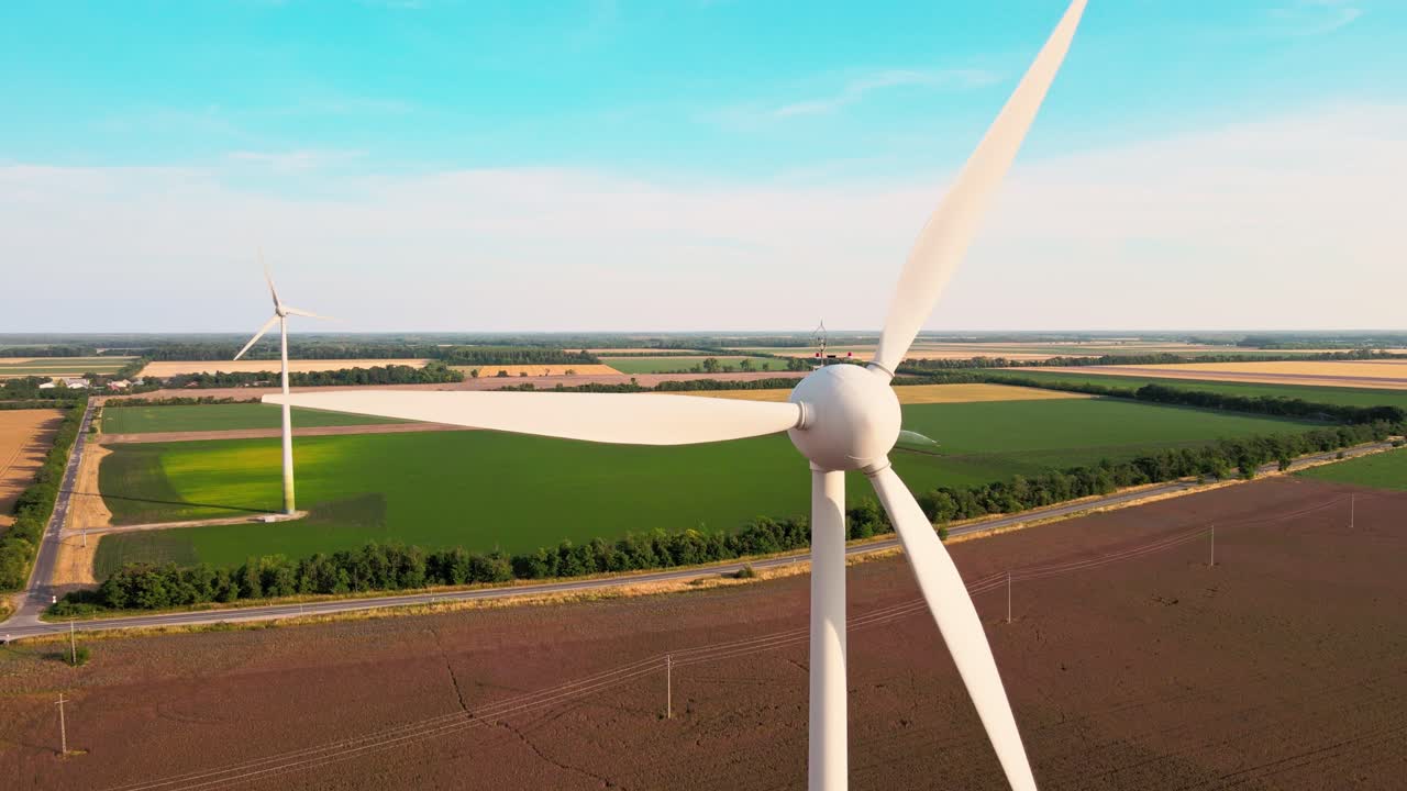 Drone che vola verso una turbina eolica in rotazione su campi agricoli verdi nell'Ungheria rurale