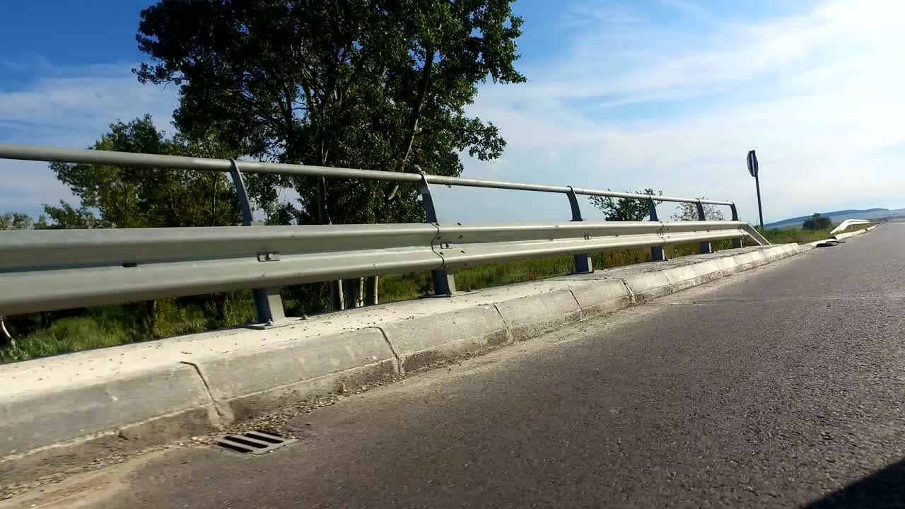 Sport pov driving on rural road with metal shield fence beside the field on a sunny day