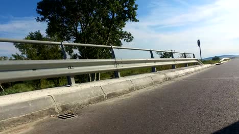 sport pov driving on rural road with metal shield fence beside the field on a sunny day