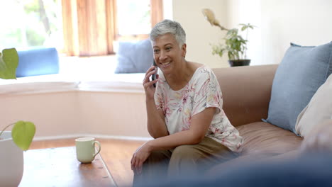 Feliz-Mujer-Birracial-Mayor-Sentada-En-El-Sofá-Y-Hablando-Por-Teléfono-Inteligente-En-Casa,-Cámara-Lenta