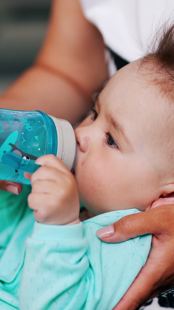 Mommy is giving a bottle with water for her baby. Cute child doesn't want to let go the bottle. Close up. Vertical video