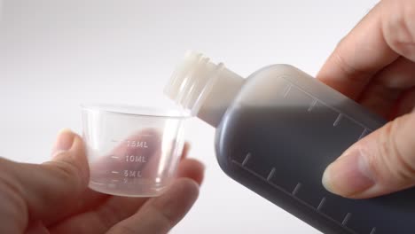 cerrar las manos femeninas vertiendo jarabe de medicina en la taza medidora de la botella para tratamientos contra la gripe