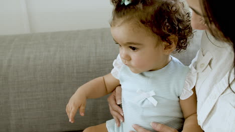 close-up of serious toddler sitting with her mom on sofa.