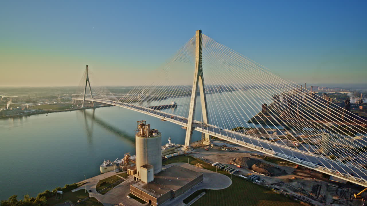 Cinematic drone shot of a Great Lakes ship cruising along the river beneath the Gordie Howe International Bridge