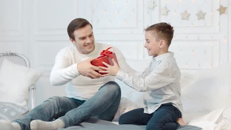 Cheerful-father-presenting-gift-to-son-in-living-room.-Boy-expressing-happiness