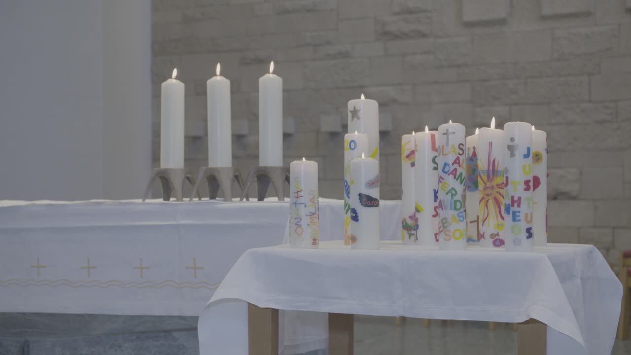 Camera pans along several burning candles on an altar and a table