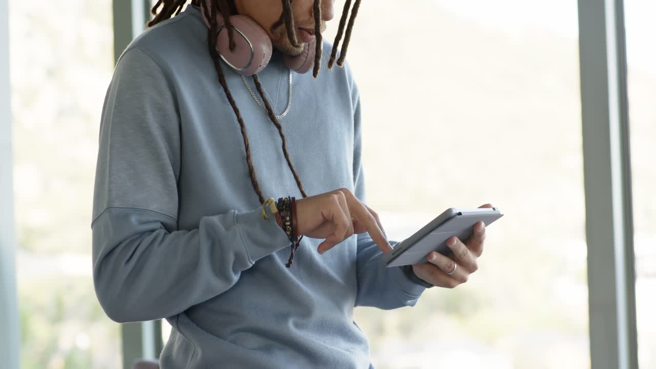 African American man tapping and swiping tablet by large window at home office browsing news