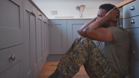 depressed male soldier in uniform suffering with ptsd on kitchen floor on home leave