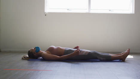 mujer caucásica en forma con máscara facial realizando yoga mientras está acostada en el estudio de yoga