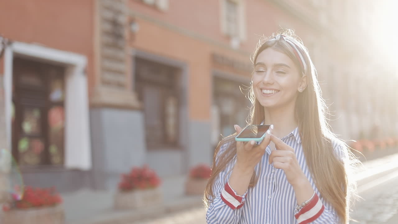 Giovane donna felice che usa l'assistente vocale sullo smartphone in città