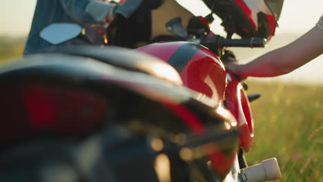 close-up of two people cleaning a red and black motorcycle in a grassy field, the motorcycle's sleek design, particularly the fuel tank, is in focus as they wipe it down