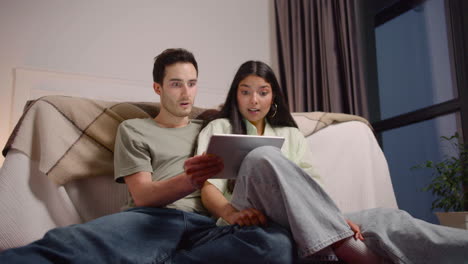 bottom view of couple watching unexpected movie scene on tablet while sitting on the floor at home