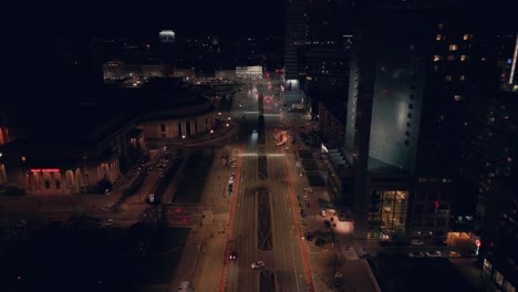 cars driving over the wide road between the high buildings at night