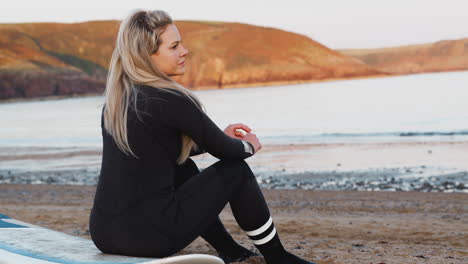 rear view of woman wearing wetsuit sitting on surfboard and looking out to sea