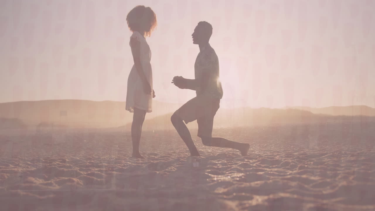 couple kneeling on beach at sunset, proposing with animated heart icon over ring box for marketing