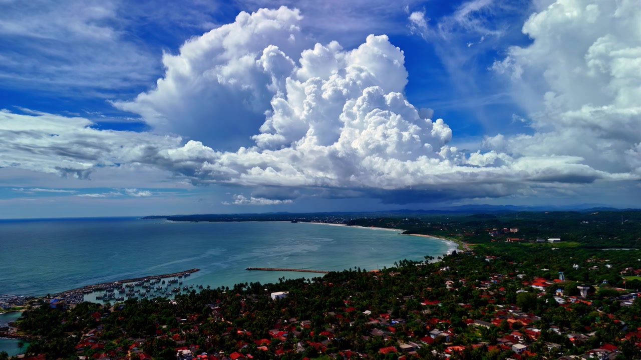 Awan badai besar terbentuk di atas teluk berjejer pohon palem Dondra dan desa pesisir saat kamera terbang di atas garis pantai