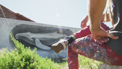 Video-of-caucasian-male-artist-with-dreadlocks-sitting-looking-at-whale-mural-on-wall