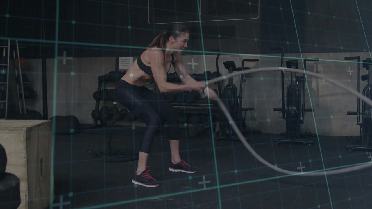 Woman doing alternating waves with battle ropes in gym, planting feet, overlay grid guiding fitness