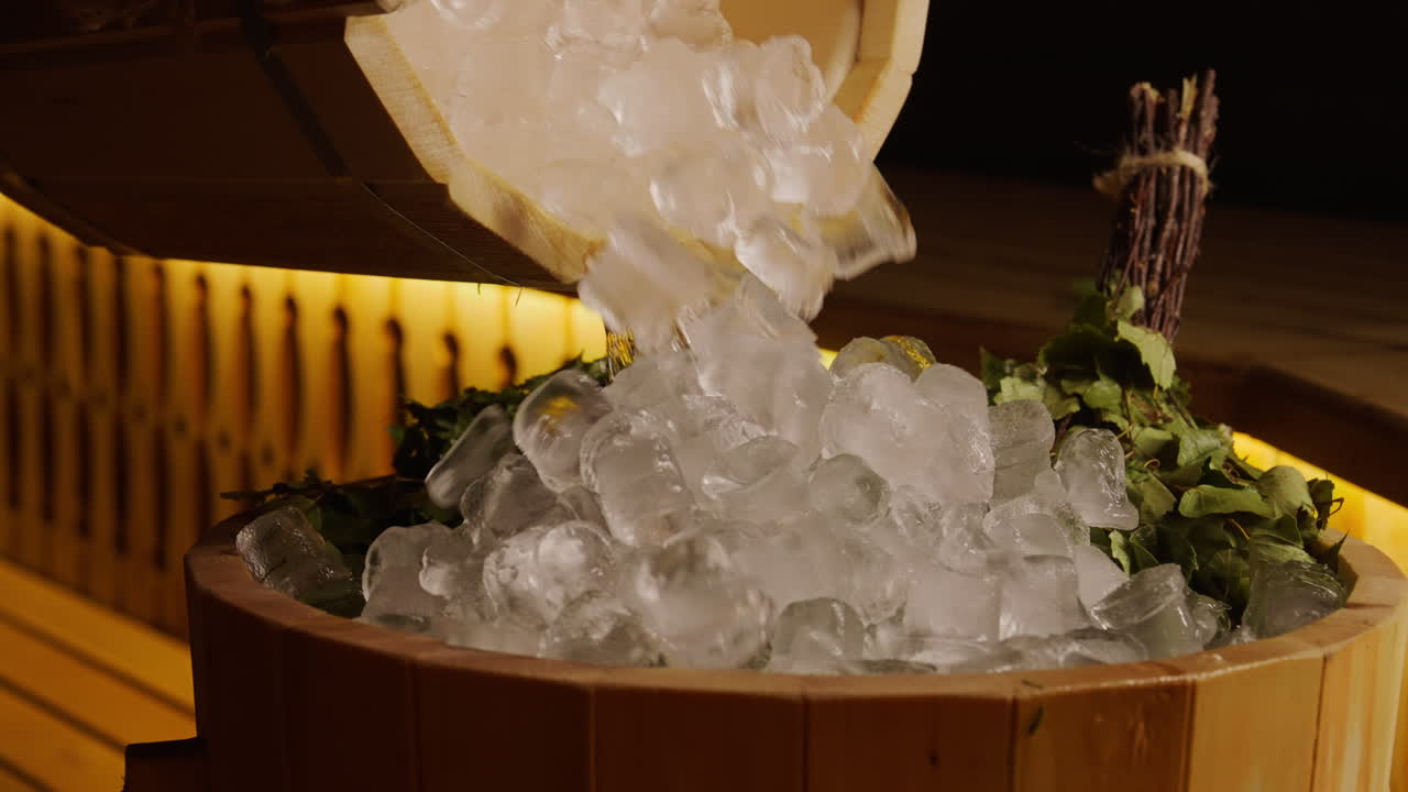 Ice being poured into a wooden sauna bucket with birch leaves