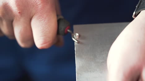 close up of hands smoothing a metal plate edge with a deburring tool