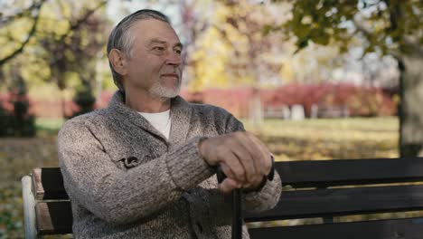 smiling old caucasian man sitting on bench in park during the autumn