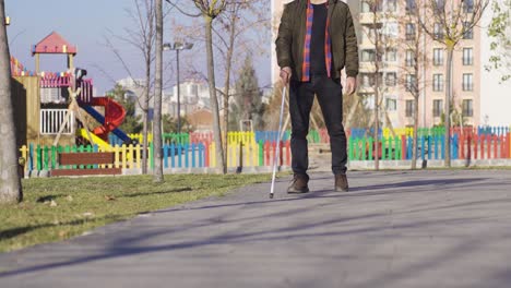 blind man walking alone in the park with the help of his cane.